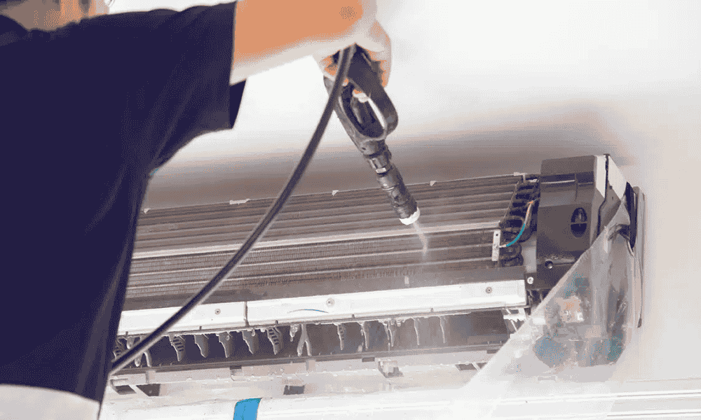 A man is performing maintenance by cleaning an air conditioning unit with a cloth.