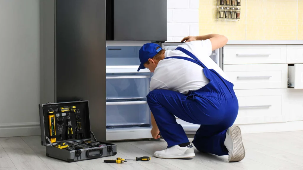 A man wearing overalls is engaged in fixing an appliance, surrounded by tools in a tidy workspace