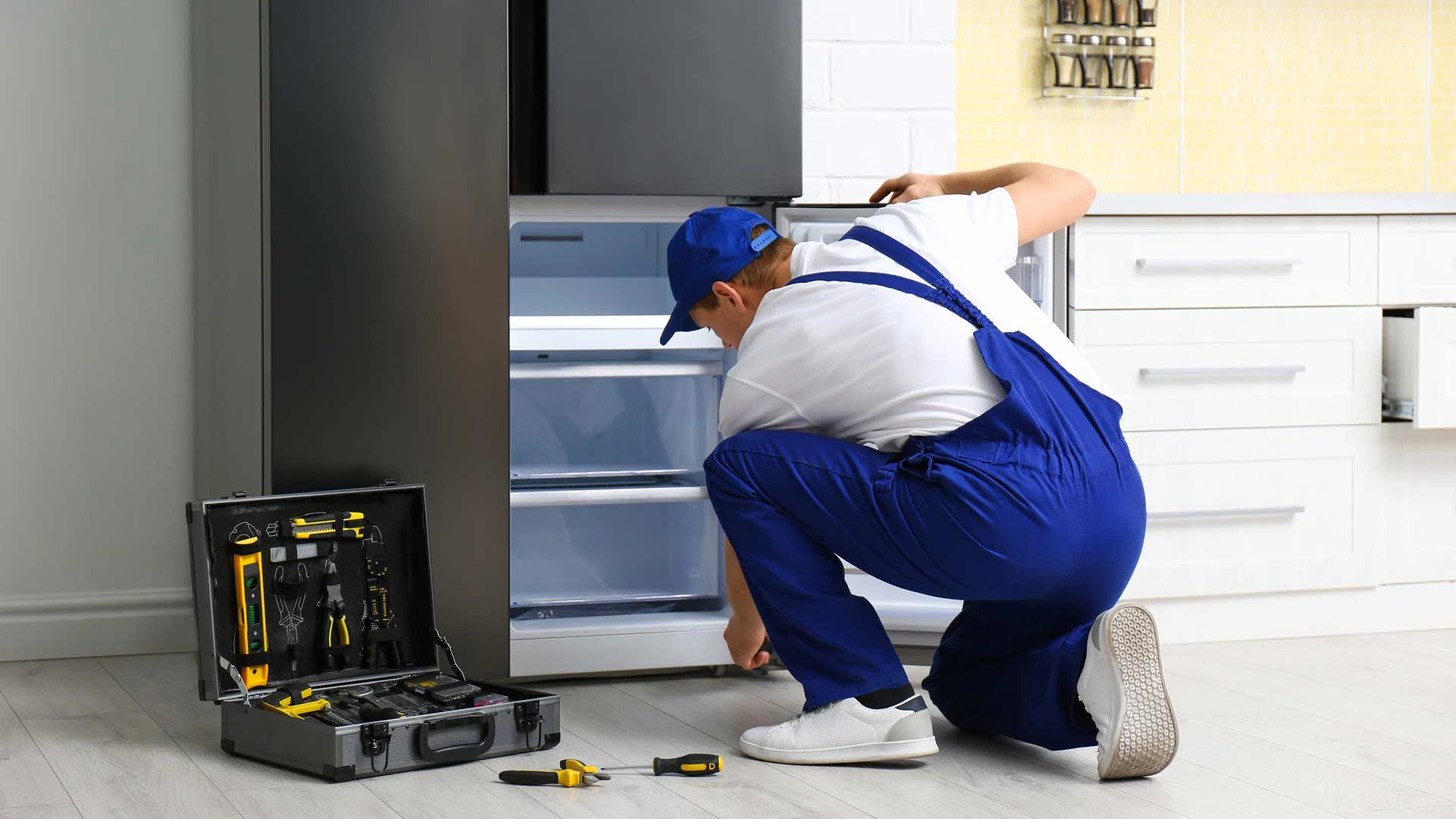 A man wearing overalls is engaged in fixing an appliance, surrounded by tools in a tidy workspace
