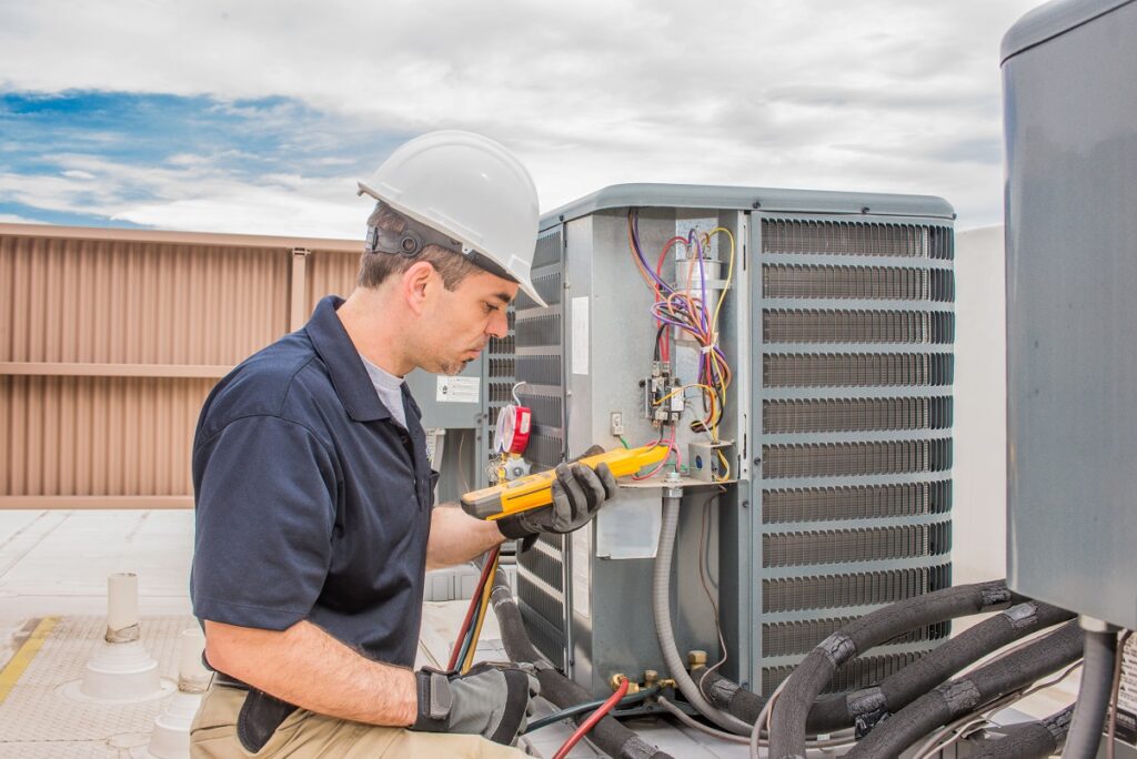 A man repairs an air conditioning unit, focused on his work with tools in hand and the unit open for maintenance.